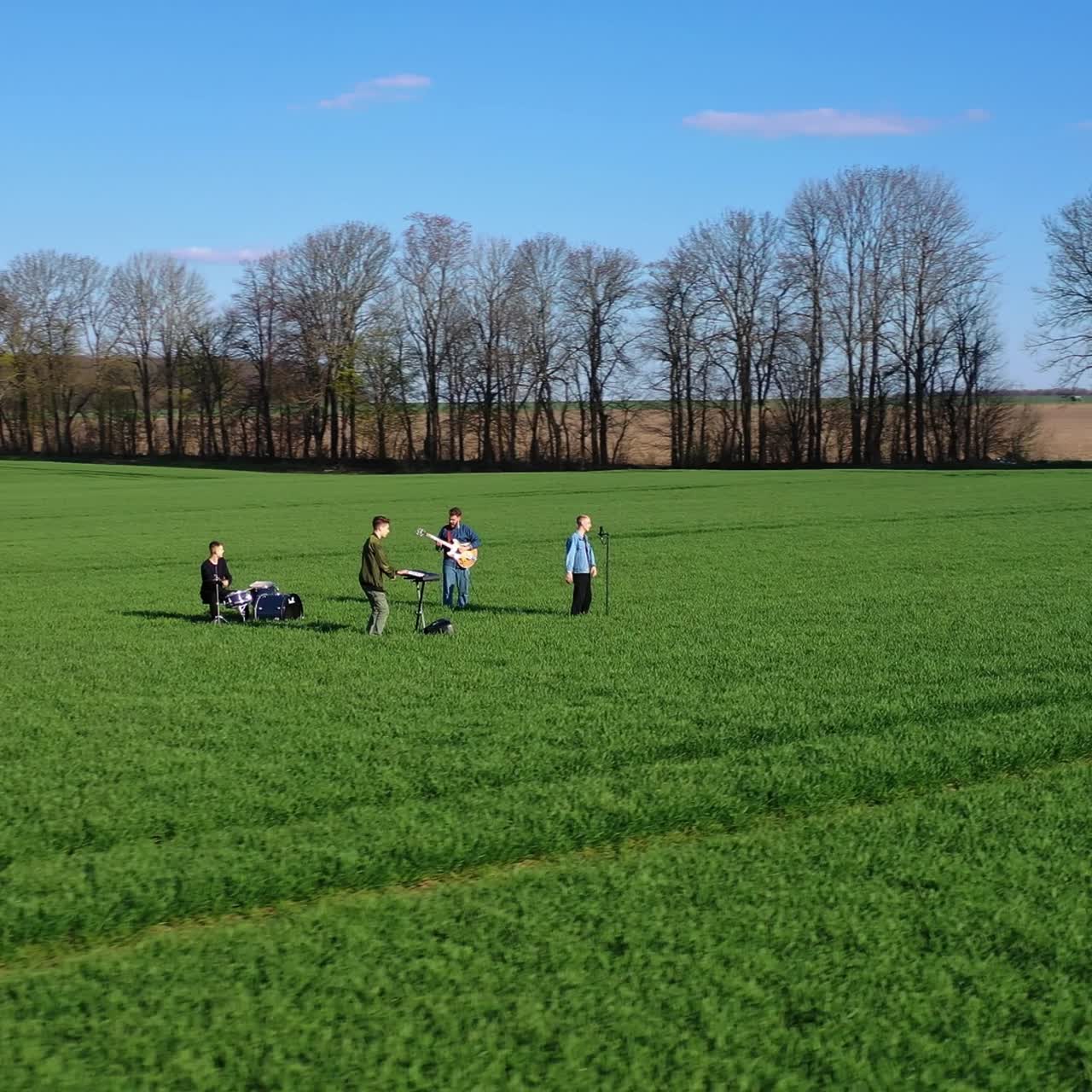 Group of young musicians on green field. Musical band performing music among nature in summer. Young people playing musical instruments. Aerial view