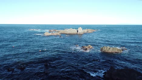 Volando-Sobre-Algunas-Rocas-En-El-Océano-Frente-A-Sinclair-Head,-Wellington,-Nueva-Zelanda