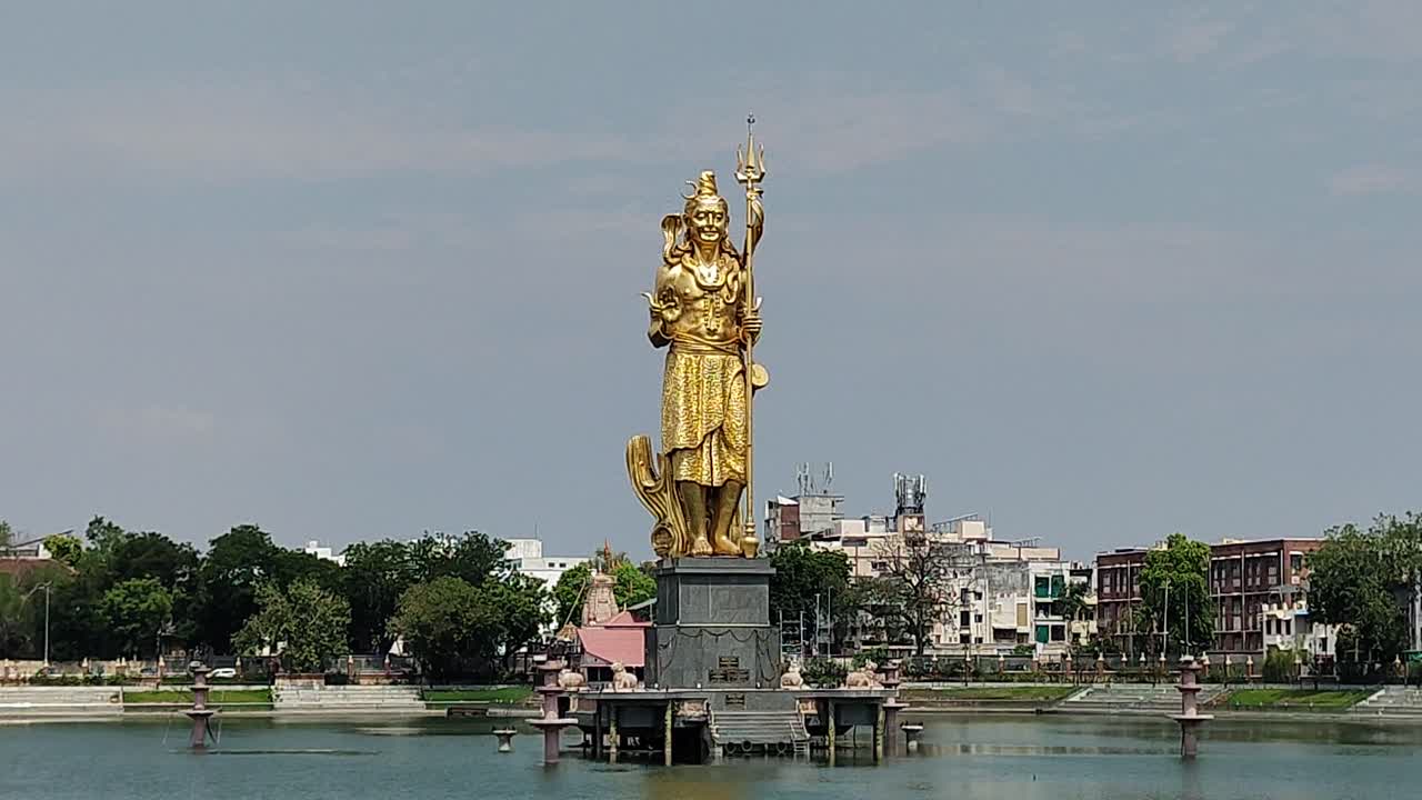 Close-up view of majestic golden Lord Shiva statue standing tall in Sursagar Lake, Vadodara, Gujarat. Sacred and iconic landmark amid urban surroundings and spiritual ambiance.