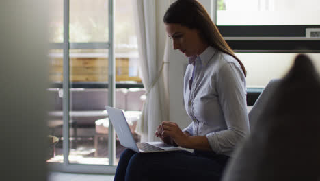 Mujer-Caucásica-Revisando-El-Papeleo-Usando-Una-Computadora-Portátil-En-La-Oficina