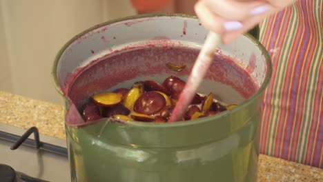 making plum jam - woman stirring plum fruits on casserole with wooden spoon in the kitchen