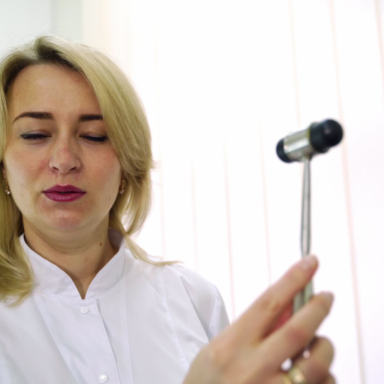 Neurology professional in white overall waving little hammer in front of the camera. Examining the reflexes at hospital