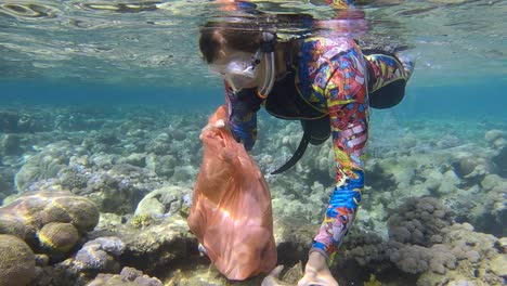 woman in diving equipment swims and collects plastic debris underwater on the bottom of coral reef. snorkeler cleaning ocean from plastic pollution. plastic pollution of the ocean (4k-60fps)