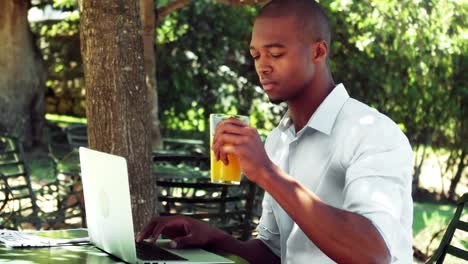 Man-drinking-juice-while-working-on-laptop