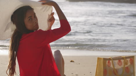 beautiful brunette latin american woman relaxing on beach takes hat off and looks with smile