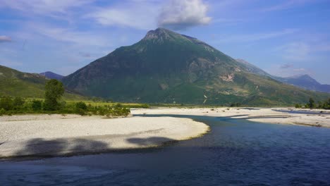 River-landscape-with-gravel,-mountain-background-and-green-hills-in-Albania