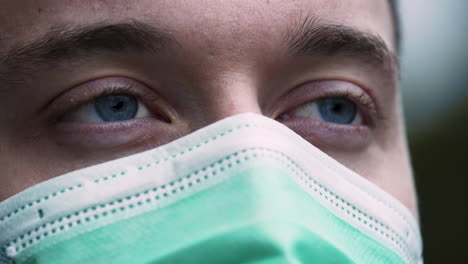 A-young-man-wearing-a-simple-green-Covid-19-protective-facemask,-slowly-opening-his-bright-blue-eyes,-looking-into-the-distance-with-hope-and-expectations,-static-close-up-4k-shot