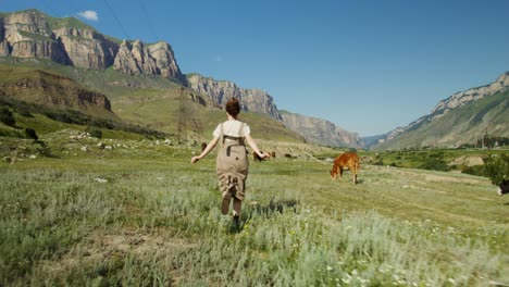 woman running through a mountain valley with cows