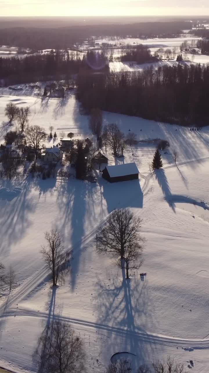 A vertical shot captures the beauty of a winter sunset over Latvia, with snow-covered houses glowing in the warm light.