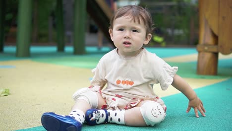 toddler asian girl playing on the playground but looking bored - adorable child wearing knee pads