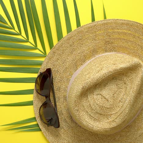 Straw-hat--green-palm-leaf-and-sunglasses-on-yellow-backdrop--Summer-concept--Flat-lay--top-view