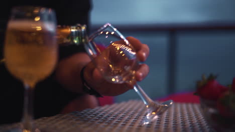 Close-up-view-of-filling-glass-with-champagne-on-the-table-with-strawberries-in-dish