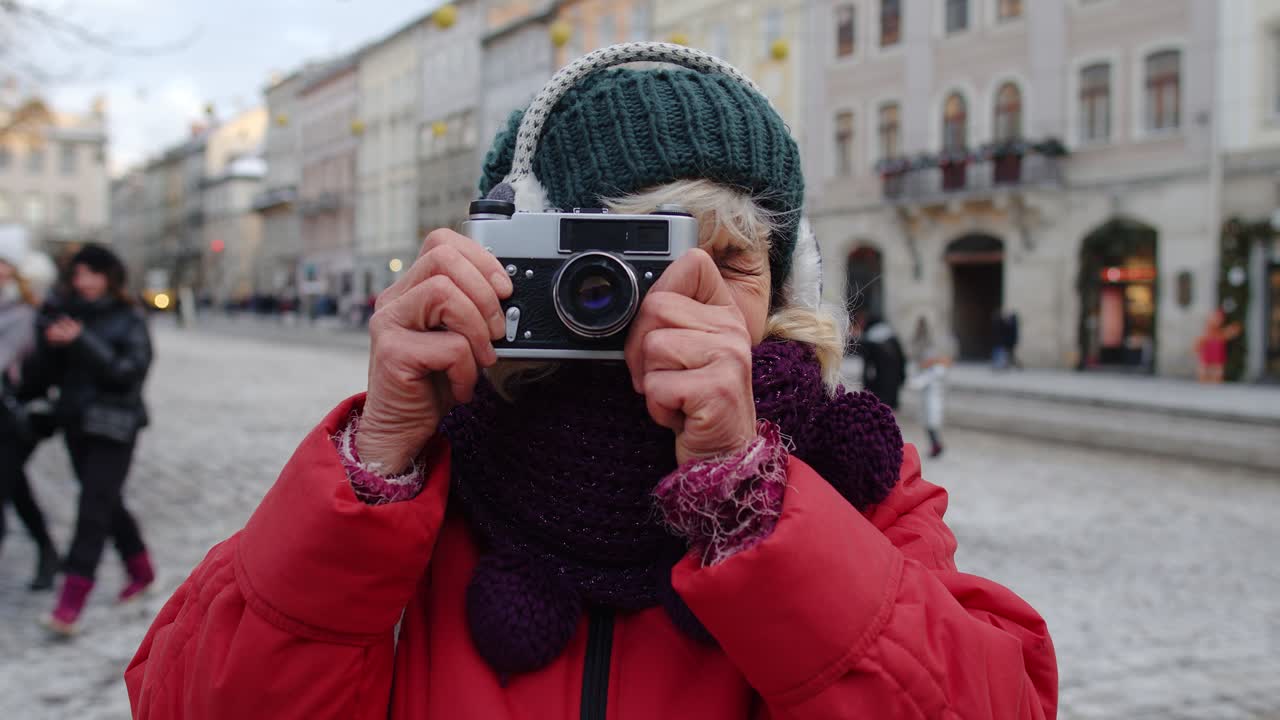 turista anciana tomando fotos con una cámara fotográfica, usando un dispositivo retro en el centro de la ciudad de invierno