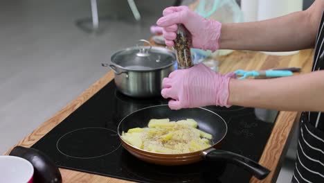 person seasoning potatoes in a frying pan on a kitchen stove
