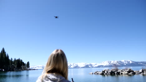 Woman-flying-drone-on-a-beach-in-Lake-Tahoe,-NV