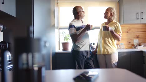 happy senior african american couple drinking coffee and talking in kitchen, slow motion