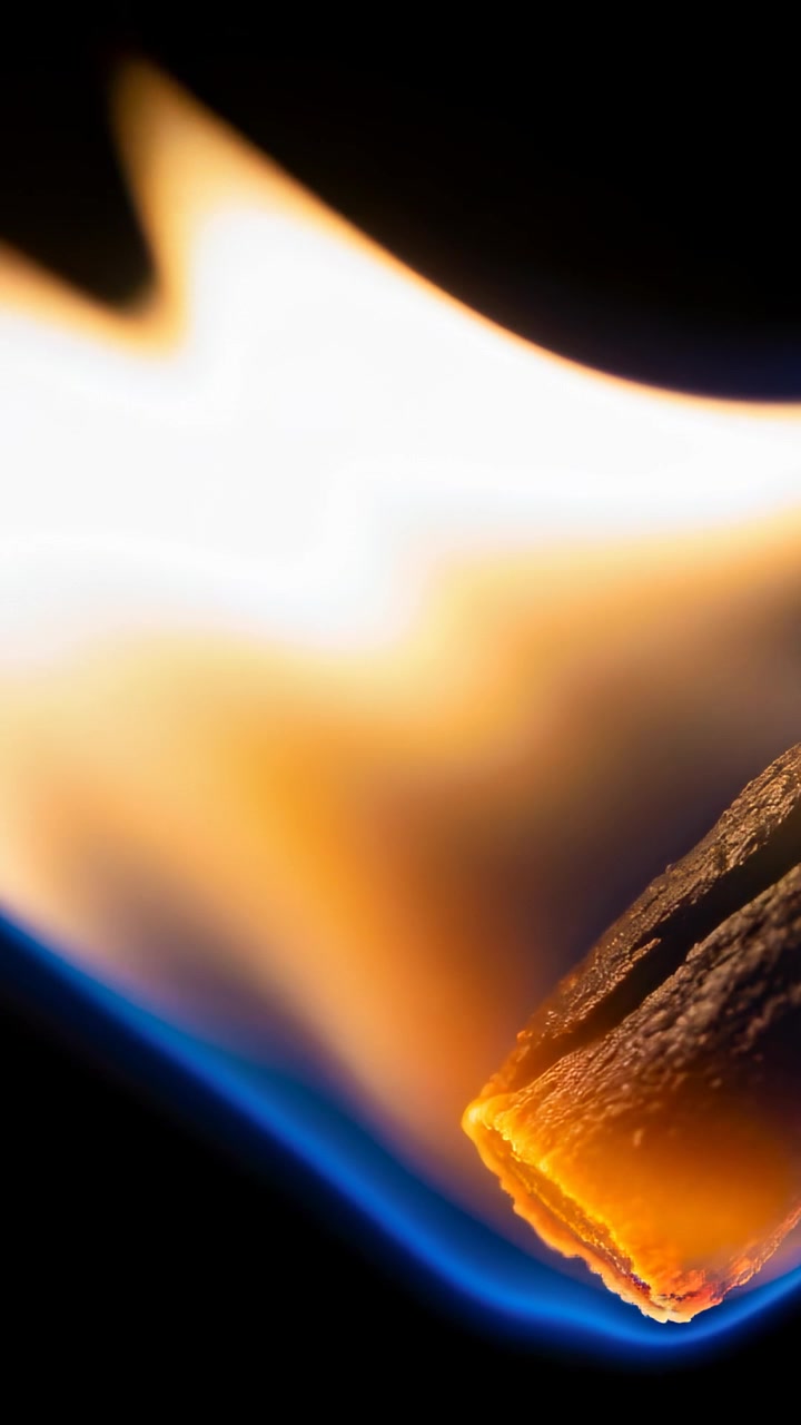 Video verticale: Fiammifero che si accende formando una base blu e una punta incandescente in uno studio buio, con il fusto carbonizzato e la brace.