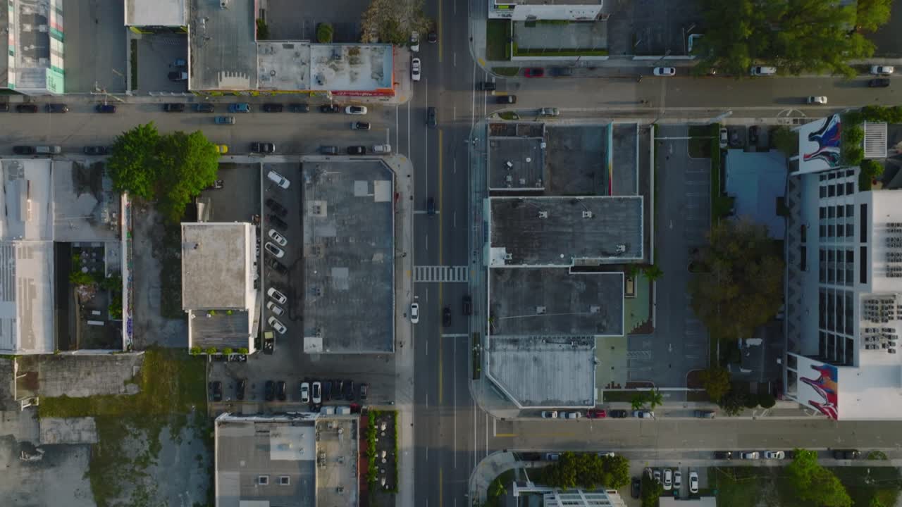 Filmagem aérea vertical de carros em ruas da cidade. Vias em área urbana ladeadas por edifícios. Miami, EUA.