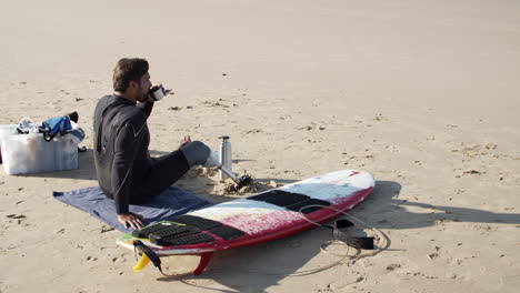 static shot of a male surfer with artificial leg drinking tea on beach