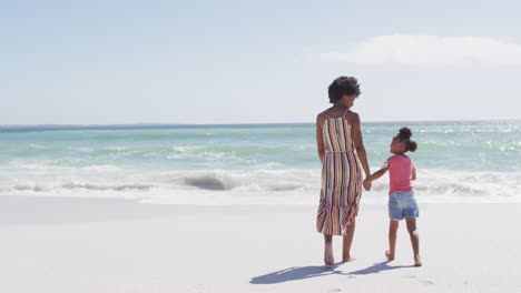 Lächelnde-Afroamerikanische-Mutter-Mit-Tochter,-Die-Am-Sonnigen-Strand-Spaziert