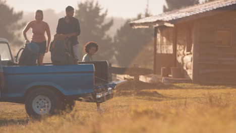 Gruppe-Von-Freunden-Entlädt-Rucksäcke-Vom-Pick-up-Truck-Auf-Dem-Roadtrip-Zu-Einer-Hütte-Auf-Dem-Land