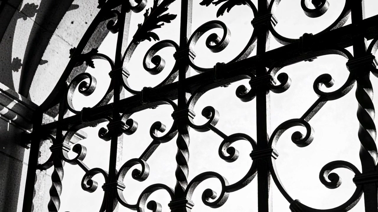 Mouvement de caméra dévoilant une grille ouvragée en fer forgé dans une ouverture en maçonnerie cintrée, présentant des motifs de feuilles.