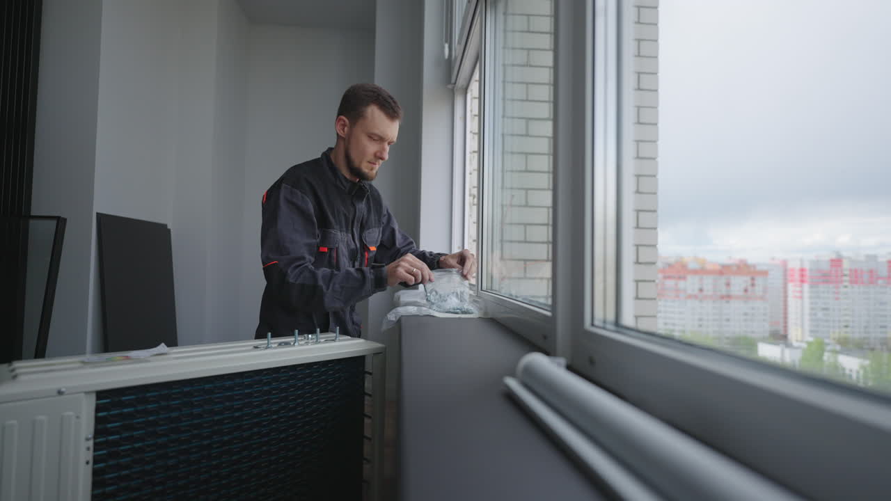 The installer is preparing to install and mount the air conditioner outside the window of the apartment at a high altitude