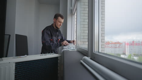 the installer is preparing to install and mount the air conditioner outside the window of the apartment at a high altitude