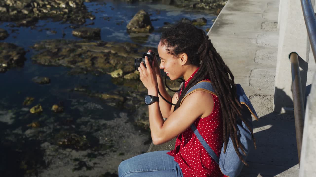 mujer afroamericana sentada y fotografiando desde el paseo marítimo