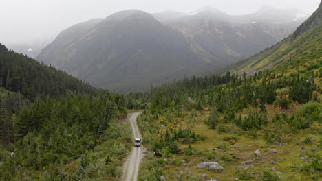 car driving on dirt road through forest valley in misty british columbia, aerial