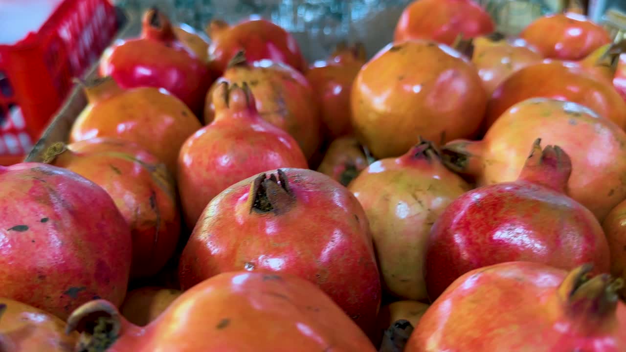 Various tropical fruits, including pomegranates, avocados, grapes, and sapodillas, arranged in red baskets under bright indoor lighting at a bustling Singapore market