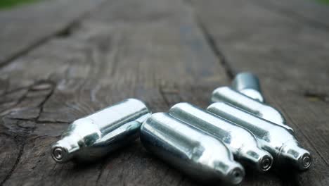 multiple chrome nitrous oxide laughing gas drug cylinders rolling across wooden park table closeup