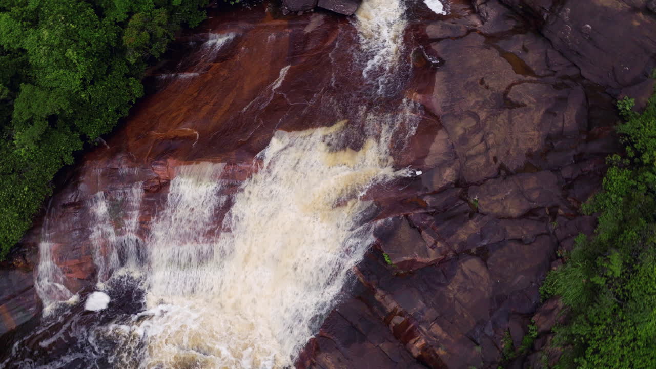 Aerial View of a Waterfall Cascading Over Red Rocks in a Lush Forest