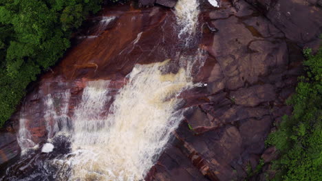 aerial view of a waterfall cascading over red rocks in a lush forest