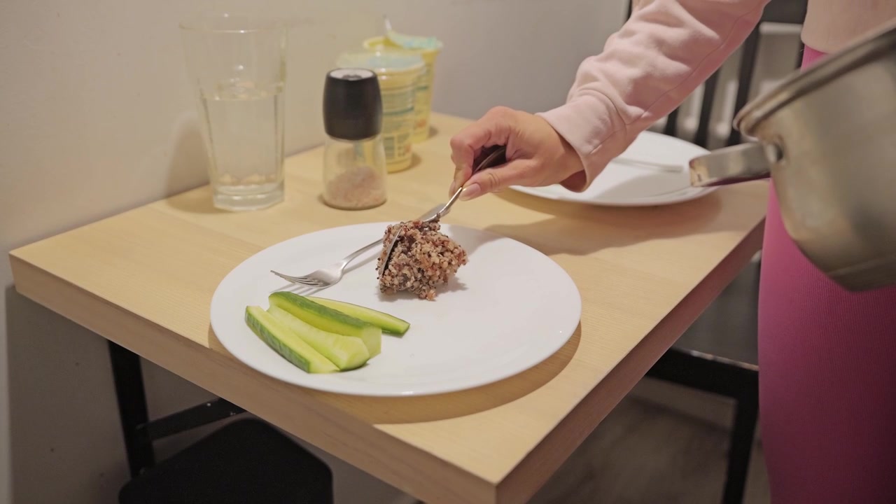 Slow motion captures serving wholesome buckwheat onto plate beside cucumber