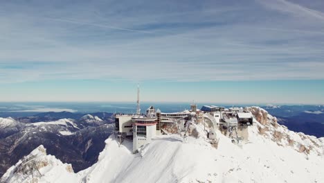 orbiting-aerial-of-snowcapped-mountain-summit-with-green-valley-below-and-mountain-ranges-in-the-background