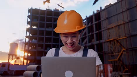 close up de una trabajadora asiática que usa gafas de protección y casco de seguridad mirando la computadora portátil y luego gritando gol celebrando mientras está de pie en el sitio de construcción