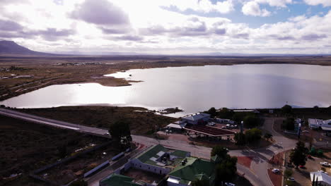 Aerial-dolly-over-Beaufort-West-toward-full-capacity-dam,-puffy-clouds-blue-sky