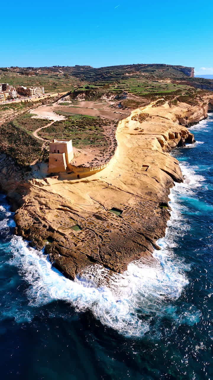 Gozo Island in Malta with a beautiful historic Xlendi Tower. White waves splash by the rocky shore. Top view. Vertical video.