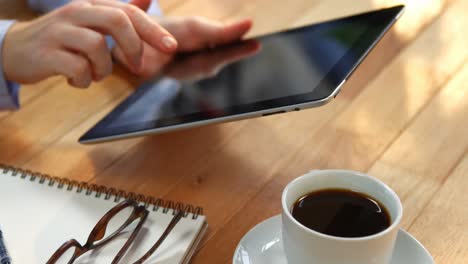 mujer de negocios usando una tableta digital en el escritorio con una taza de café, gafas y cuaderno en la mesa