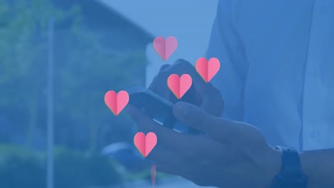 animation of hearts floating over hands of caucasian man using smartphone