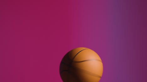 close up studio shot of male basketball player spinning ball on finger against pink lit background