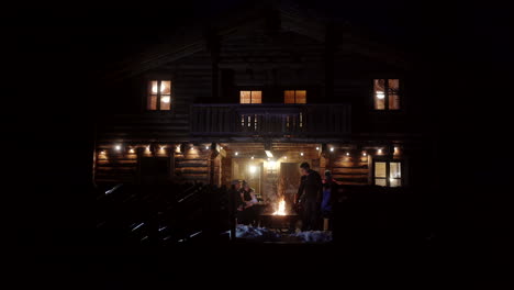 friends gathered around a bonfire at a log cabin in the snowy night