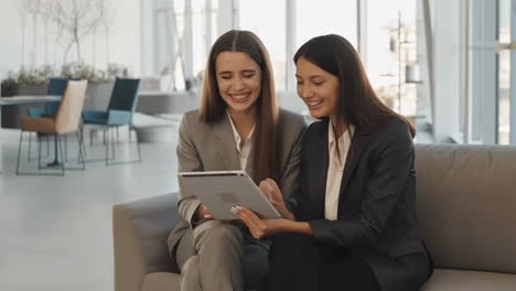 two businesswomen collaborating and smiling while using a tablet in an office setting