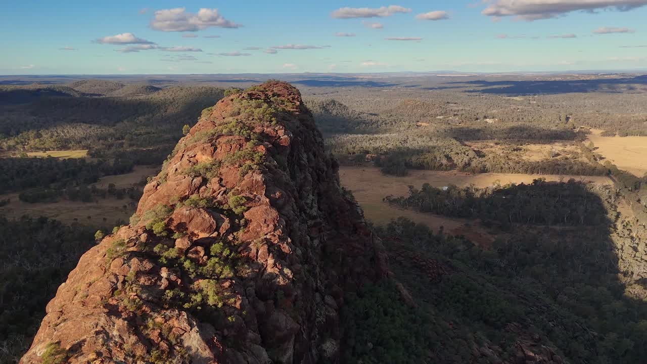 Drone glides above Timor Rock’s rugged ridge in Coonabarabran, revealing dramatic rock formations, expansive bushland, and golden hour lighting with sweeping camera movement