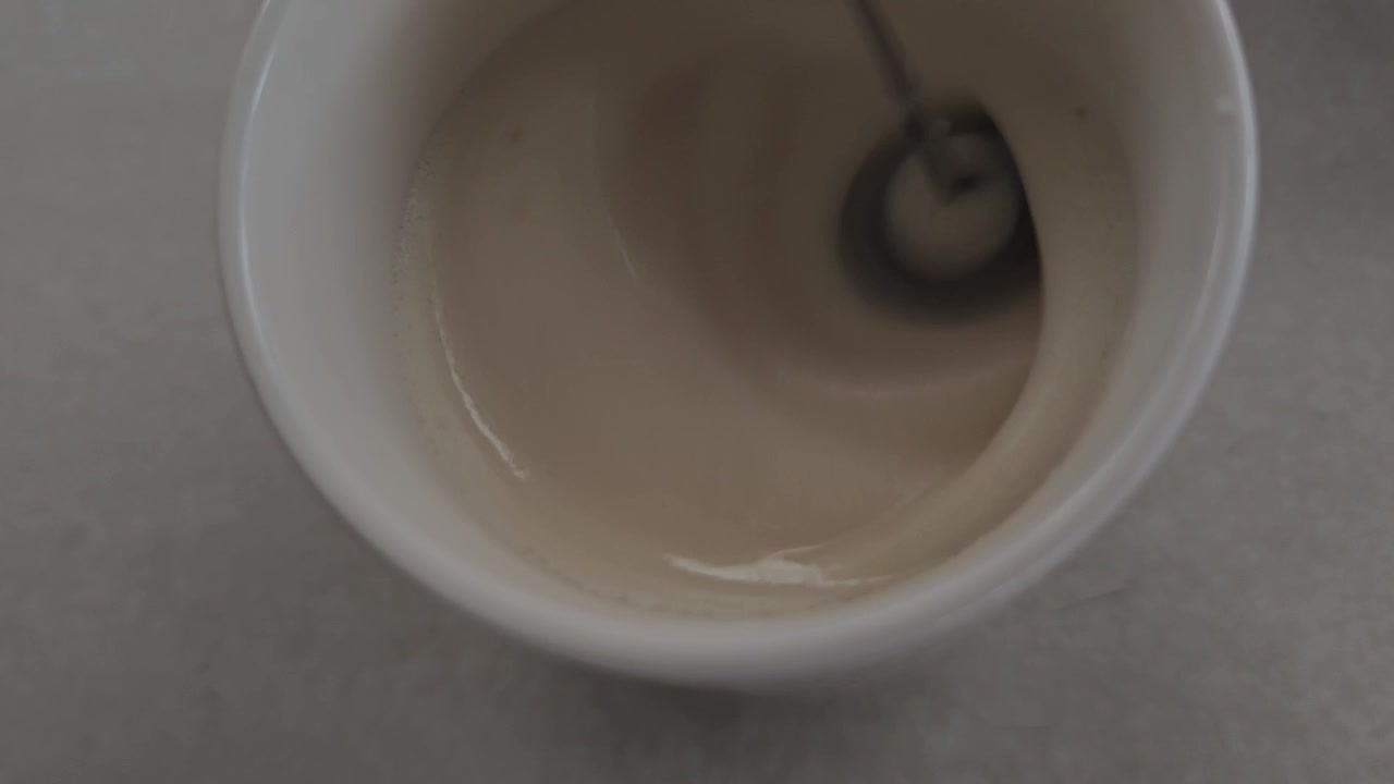 Schiumatura al rallentatore di latte di soia in tazza bianca, incantevoli spirali di schiuma e piccole bolle cremose create da un frullino ad alta velocità, estetica accogliente da barista per caffè, caffetterie, bevande benessere all'alba!!!