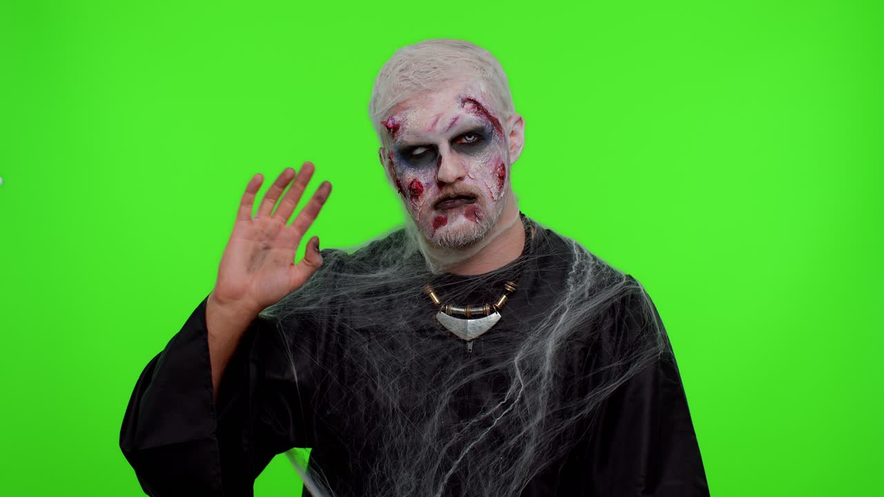 Creepy Halloween zombie man smiling friendly waving hands gesturing hello or goodbye, welcoming