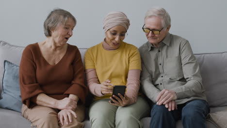 Vista-Frontal-De-Una-Mujer-árabe-Enseñando-A-Una-Anciana-Y-A-Un-Hombre-A-Usar-Un-Teléfono-Inteligente