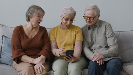 vista frontal de una mujer árabe enseñando a una anciana y a un hombre a usar un teléfono inteligente