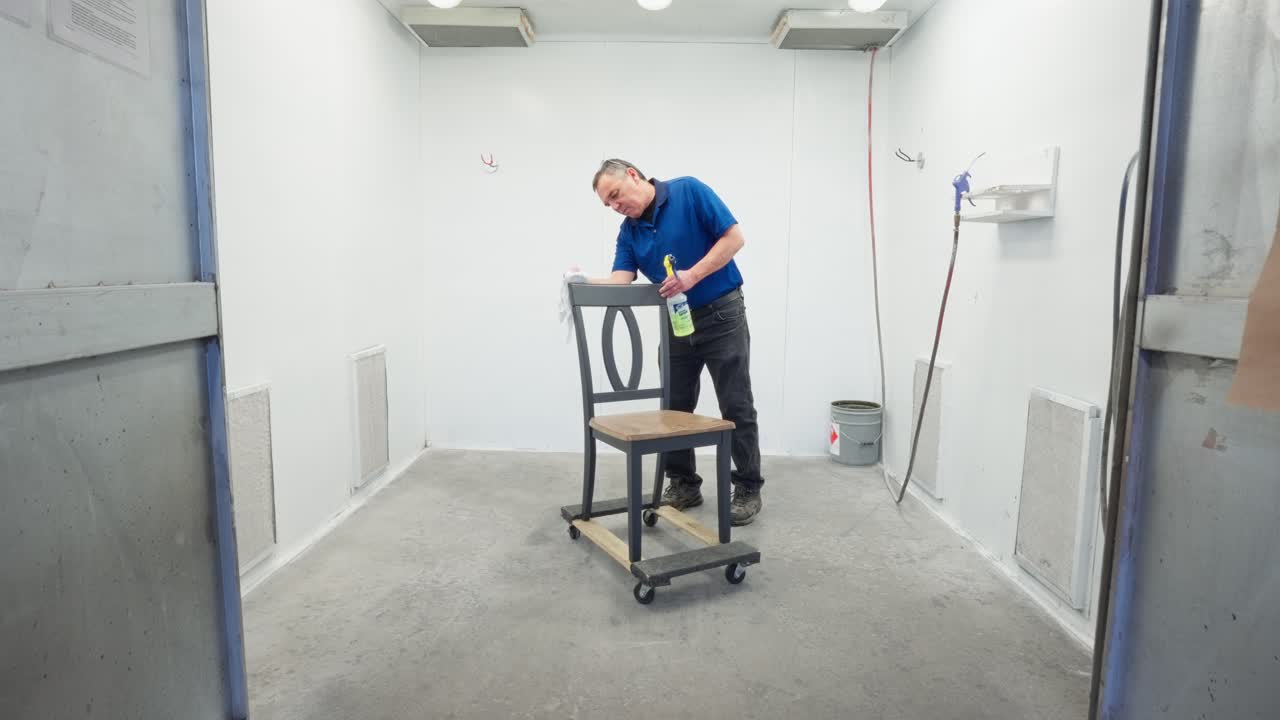 Camera pushes in in slow motion as worker cleans wooden chair with spray and rag